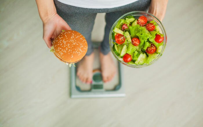 woman measuring body weight on weighing scale holding burger and salad sweets are unhealthy junk food dieting healthy eating lifestyle weight loss obesity top view